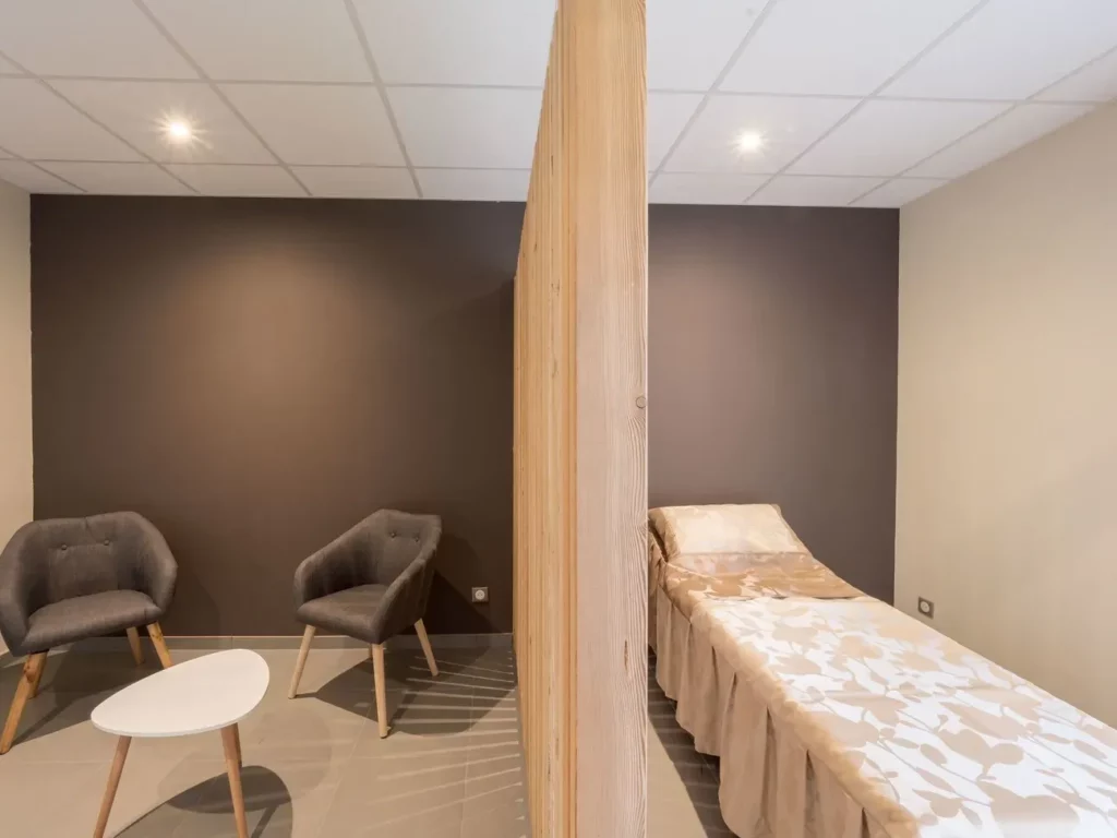 Espace de recueillement intime avec lit funéraire et coin salon séparé par un claustra.