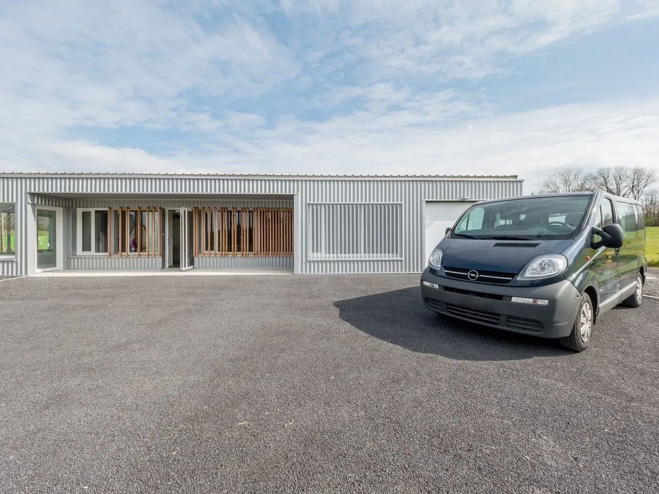 Fourgon funéraire garé devant le bâtiment moderne à bardage métallique.
